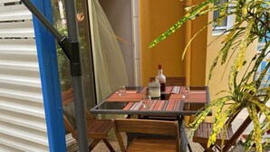 En udendørs terrasse med et bord, stole, en potteplante og en skydedør.