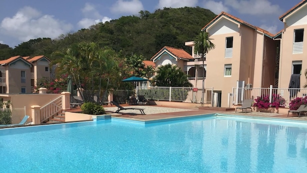 En swimmingpool med liggestole, et lille overdækket siddeområde og et bjerg i baggrunden.