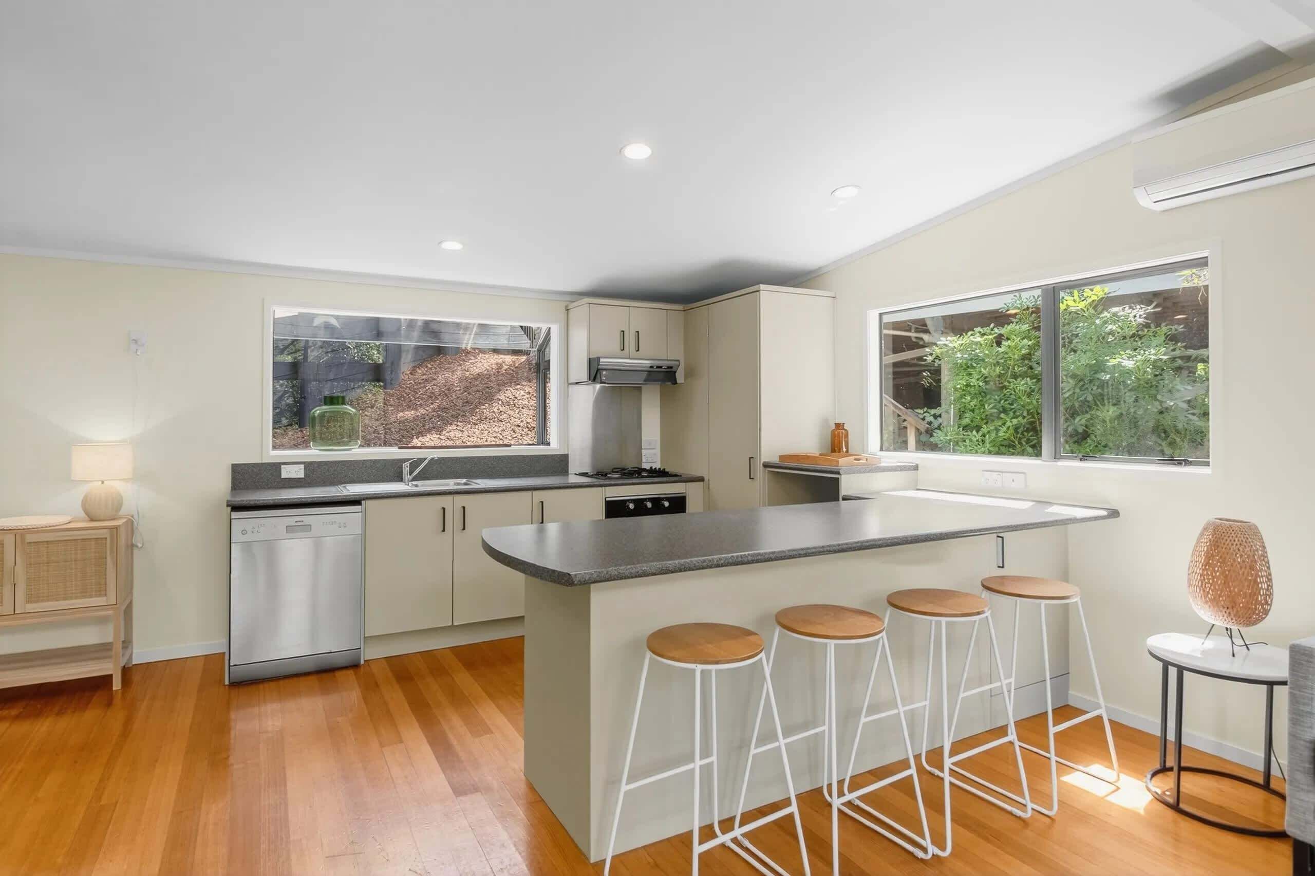 A modern kitchen with a central island, bar stools, and a dishwasher.