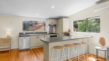 A modern kitchen with a central island, bar stools, and a dishwasher.