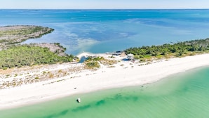 Vista aérea de una playa con aguas turquesas cristalinas, una orilla de arena y varios edificios de diseño circular.