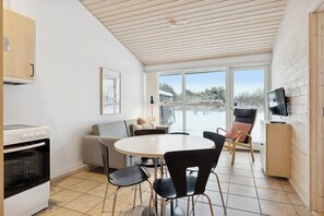 A kitchen with a stove, a dining table with chairs, a sofa, and a TV on a stand. - Apartment near the sea with calm and life (Pandrup)