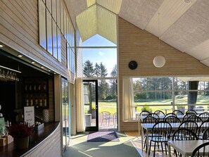 Un restaurante con zona de bar, mesas al aire libre y amplios ventanales con vistas a un campo de golf.
