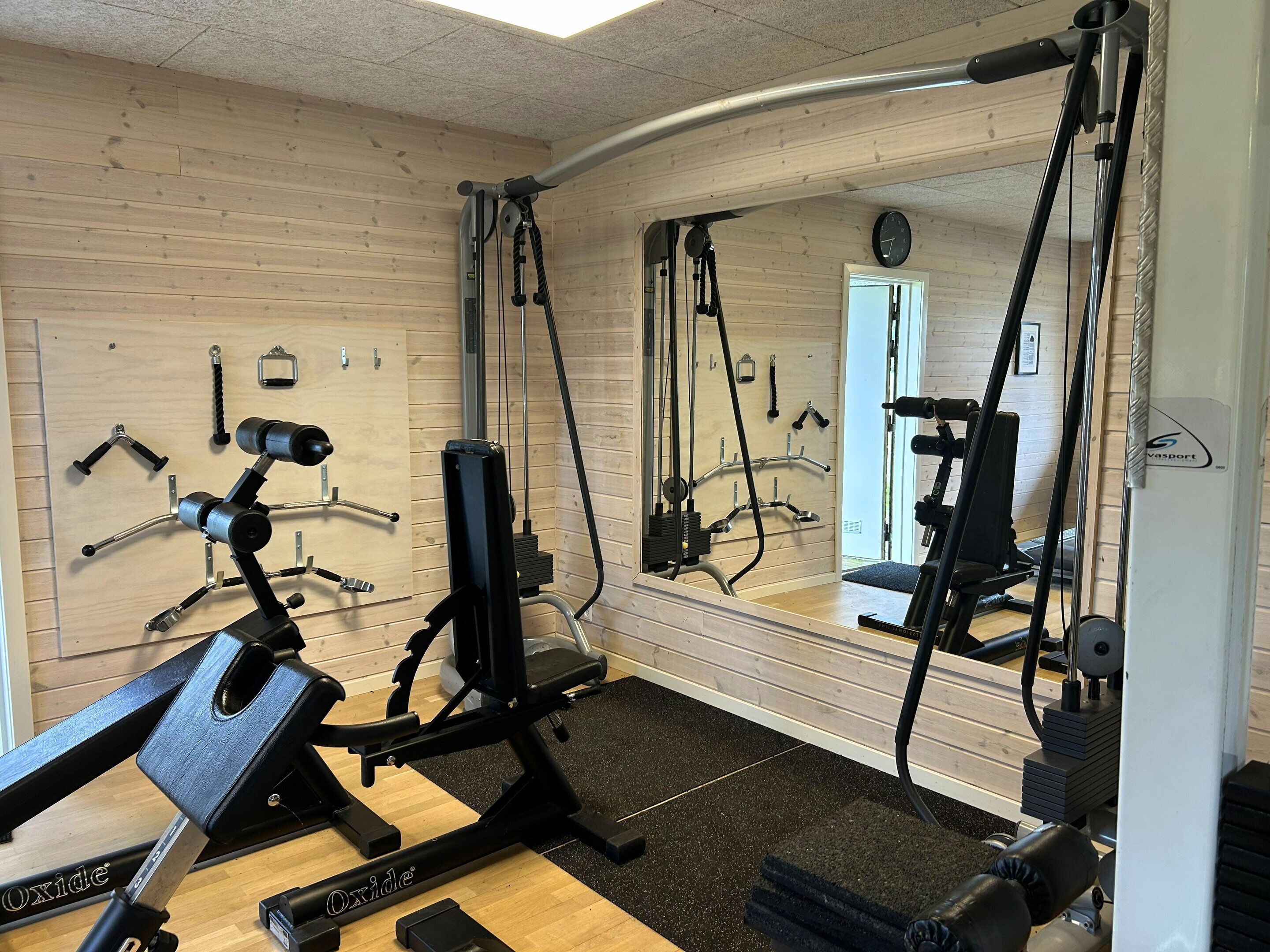 Ein Fitnessraum mit Trainingsgeräten, Holzwänden und einem Spiegel.