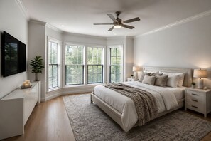A bedroom with a large bed, bedside lamps, a ceiling fan, and a view through the windows. - Masters Week Golf Estate / 6BR + Private Entry Apartment / Sleeps 12 / Fire Pit (Aiken)
