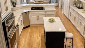 Une cuisine moderne avec un plancher en bois, des meubles blancs, un îlot central et un coin repas baigné de lumière naturelle.