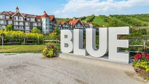 A sign with the word "BLUE" in large letters, set against a backdrop of traditional buildings and a green landscape. - Grand 8-Bedroom Retreat, 7 Baths - Perfect Chalet (The Blue Mountains)