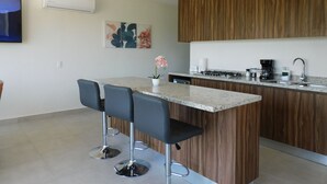 Eine moderne Küche mit einer zentralen Kochinsel, Barhocker, einem eingebauten Herd und einer Kaffeemaschine.