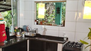 A kitchen with a central island, two bar stools, a gas stove, and a window with a view of greenery. - House in Serra do Piloto with natural pool, waterfall runs throughout the property. (Vila Muriqui)