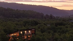 Una cabaña en un bosque con vista al atardecer.