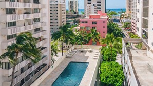 Um hotel moderno com piscina no terraço, palmeiras e vista para o oceano.