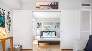 Quarto moderno com cama, mesas de cabeceira e vista para a cidade através de uma porta aberta.