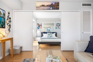 Ein modernes Schlafzimmer mit Bett, Nachttischen und Blick auf die Stadt durch eine offene Tür.