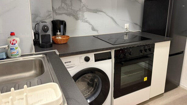 Uma cozinha compacta com máquina de lavar, forno, cafeteira e pia.