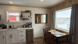 A kitchen with a sink, coffee makers, and a dining table with chairs. - Cabane du quai Vacation Home (Chéticamp)
