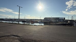 A marina with boats docked, a large industrial building, and a clear sky. - Cabane du quai Vacation Home (Chéticamp)