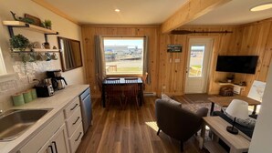 A wooden interior with a kitchen, dining area, and seating space. - Cabane du quai Vacation Home (Chéticamp)