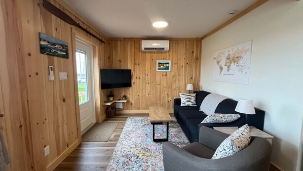 A wooden-paneled room with a sofa, a coffee table, a TV, and a map on the wall. - Cabane du quai Vacation Home (Chéticamp)