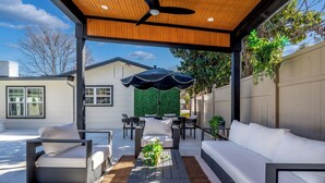 Eine Terrassengruppe im Freien mit Deckenventilator, schwarzem Sonnenschirm und einer Sitzecke mit weißen Sofas und Sesseln.
