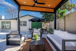 An outdoor patio with a ceiling fan, a black umbrella, and a seating area with white sofas and chairs. - Relaxed Luxury Pet Friendly Home w/ Pool & Backyard Lounge in San Antonio, Tx (San Antonio)