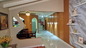 A hallway with a marble wall, wooden paneling, and a ceiling fan. There are shelves with decorative items and a framed picture on the wall. - Cozy & Secure 2BR Old Harbour Retreat: All the Comforts of Your Own Home (St.Catherine)