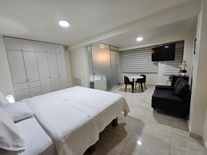 Ein Hotelzimmer mit einem Bett, einem Schreibtisch, einem Sessel, einer Couch und einem Fernseher.