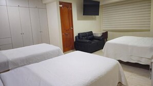 Ett hotellrum med två sängar, en garderob, en soffa, en TV och ett fönster med persienner.