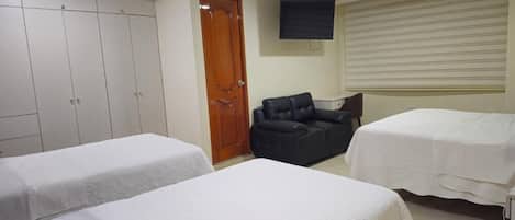 A hotel room with two beds, a wardrobe, a sofa, a TV, and a window with blinds.