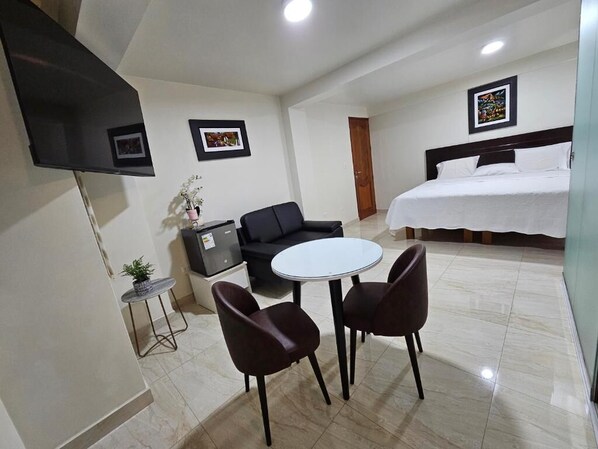 Ein Hotelzimmer mit einem Bett, einem an der Wand befestigten Fernseher, einem kleinen Tisch mit zwei Stühlen und einer Zimmerpflanze.