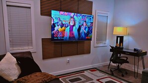 Un salon doté d’un téléviseur à écran plat fixé au mur, d’un canapé en cuir, d’un bureau avec une chaise et d’un tapis à motifs.