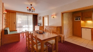 A cozy room with a wooden dining table, chairs, a sofa, a television, and a kitchen area with cabinets and a microwave. - R Sidence Le Cabourg St4n (Les Deux Alpes)