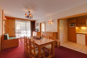 Ein gemütliches Zimmer mit Holztisch, Stühlen, einer Sitzecke, einem Fernseher und einer Küchenzeile mit Schränken und einer Mikrowelle.