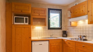 A kitchen with wooden cabinets, a microwave, a dishwasher, a window, and a coffee maker. - R Sidence Le Cabourg St4n (Les Deux Alpes)