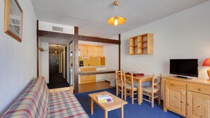 A room with a sofa, a dining table with chairs, a television, and a kitchen area. - R Sidence Le Cabourg St4n (Les Deux Alpes)