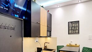 A compact kitchen with a built-in washer and dryer, a small dining area with a green chair, and a flat-screen TV mounted on the wall. - Petit Palace (Beograd)
