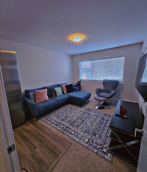 A living room with a sectional sofa, a small armchair, a coffee table, and a rug. - ATARE Lush family-friendly apartments (Saskatoon)