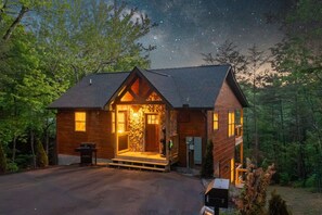A cabin with a stone facade, a wooden deck, and a starry night sky. - Mountain Views, Hot Tub, Game Room & Deck (Sevierville)
