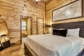 Ein Schlafzimmer einer Holzhütte mit einem Bett, einer Karte an der Wand und Blick ins Freie.