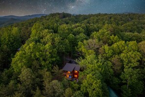 Eine Hütte, umgeben von dichtem Wald, mit einem sternenübersäten Nachthimmel.