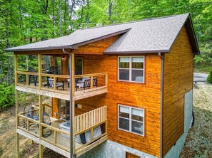 A two-story wooden cabin with a balcony on the upper level, surrounded by trees. - Mountain Views, Hot Tub, Game Room & Deck (Sevierville)