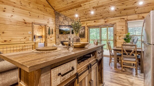 A wooden cabin interior with a kitchen island, dining area, and a stone wall. - Mountain Views, Hot Tub, Game Room & Deck (Sevierville)