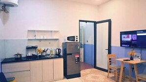 A compact kitchen with a refrigerator, microwave, and coffee maker. There is a small dining area with a table and chairs. - Yuki Hanoi Center Apartment (Hanoi)