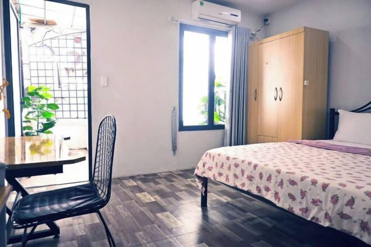 Une pièce comprenant un lit, une armoire en bois, une table à manger avec une chaise, une fenêtre avec des rideaux et une plante en pot.