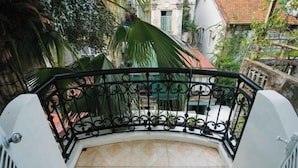 A curved balcony with a black wrought iron railing, surrounded by greenery and buildings with red-tiled roofs. - Yuki Hanoi Center Apartment (Hanoi)