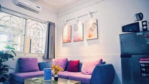 A modern living room with a purple sofa, a glass coffee table, and a wall-mounted air conditioner. - Yuki Hanoi Center Apartment (Hanoi)