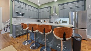 A modern kitchen with grey cabinets, a stainless steel refrigerator, and wooden bar stools. - Over-the-Rhine, 4 Bedroom, Game Room, Grill & Patio (Cincinnati)