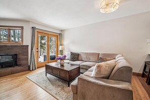 A living room with a sofa, a coffee table, a fireplace, and a window with a view of trees. - Rivera's Run: Dog Friendly Frisco Townhome, Gas Fireplace, Walk to Downtown (Frisco)