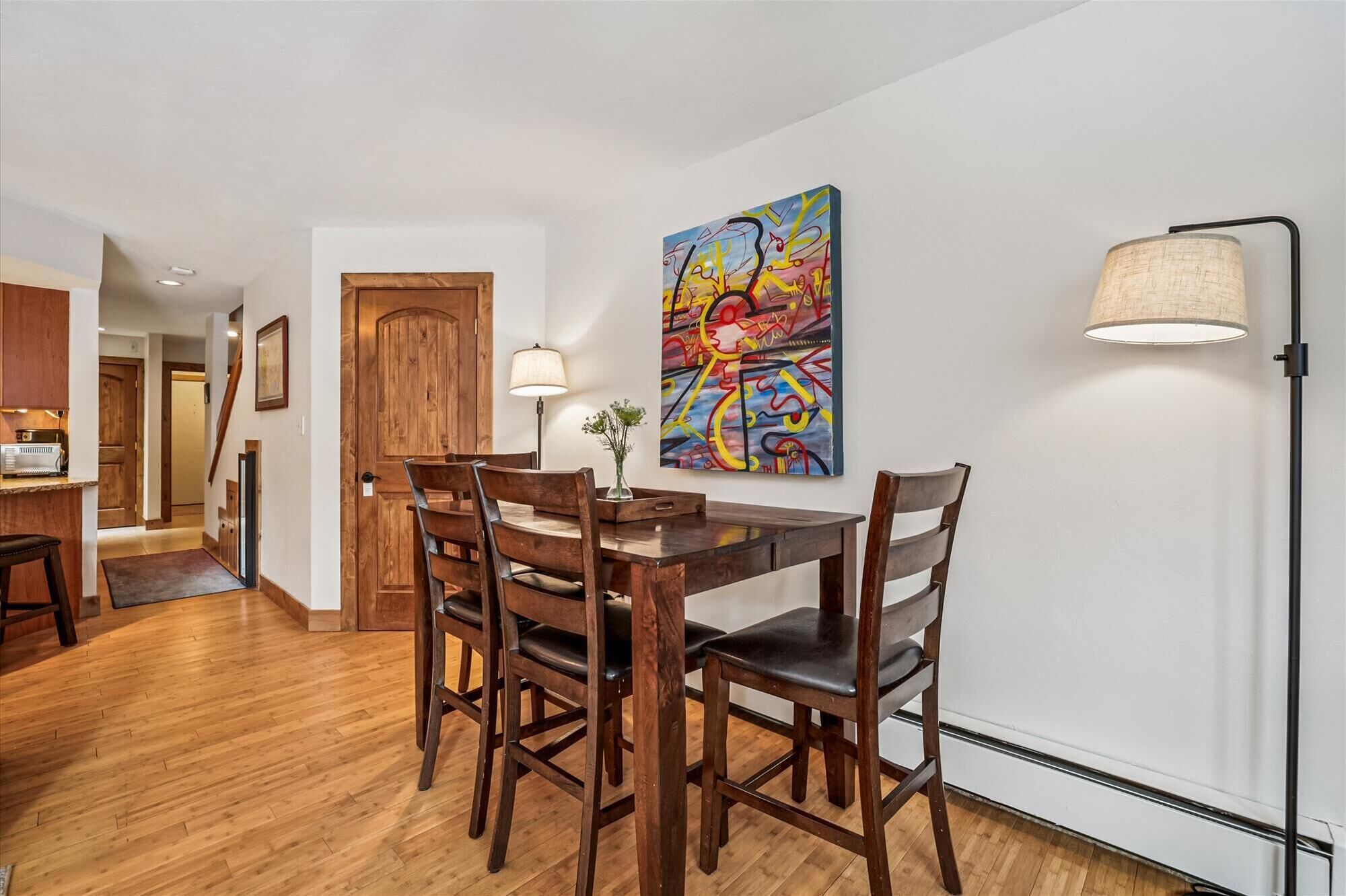 Un coin repas avec une table et des chaises en bois, une peinture abstraite aux couleurs vives accrochée au mur et un lampadaire.