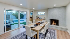 A modern dining area with a large table set for six, a fireplace, and a view of the backyard. - New! Modern Home on Mill Ave. Pool. Pet Friendly. (Tempe)