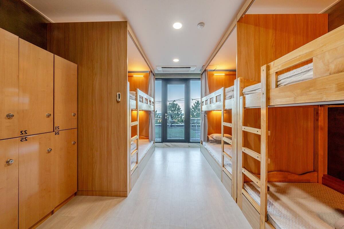 Un pasillo con literas, taquillas de madera y una puerta de vidrio que da al exterior.